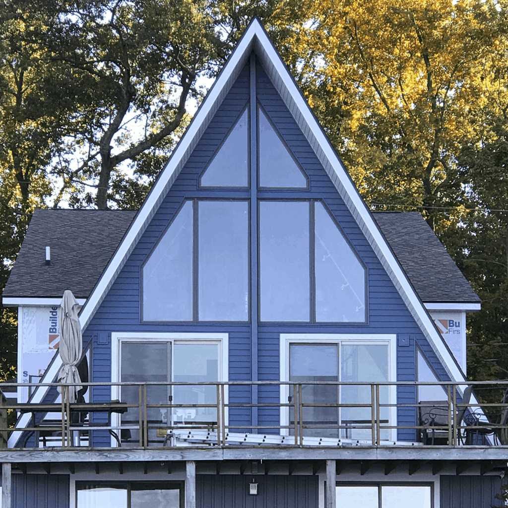 Striking blue A-frame lakeside home in Michigan with large glass windows, upper deck, and wooded waterfront setting