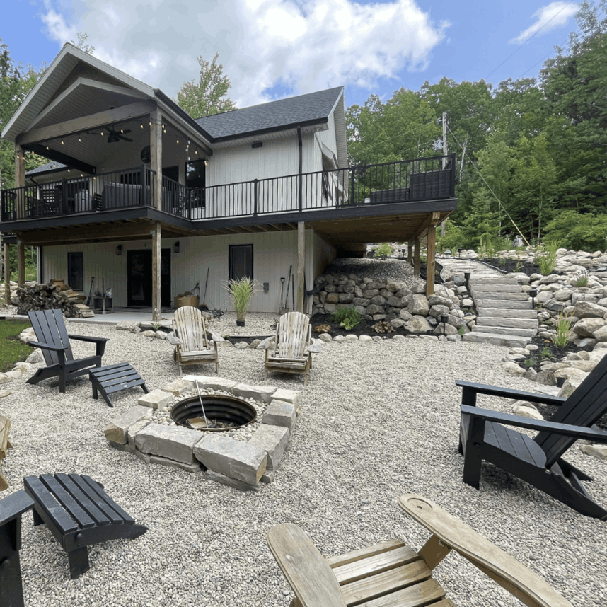 Spacious backyard remodel of a West Michigan lake home with large deck, string lights, Adirondack chairs, and stone fire pit area
